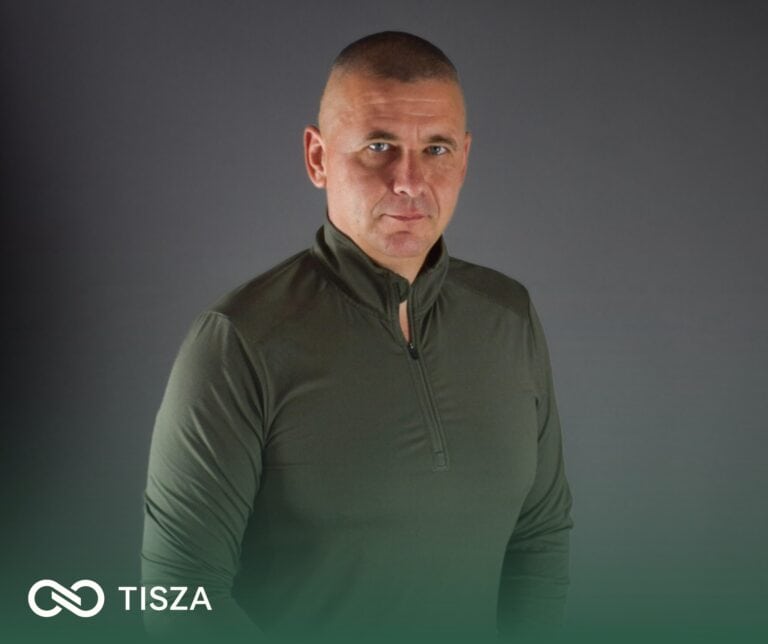 Halványkék sportos ruha, rövid haj, komoly arckifejezés.