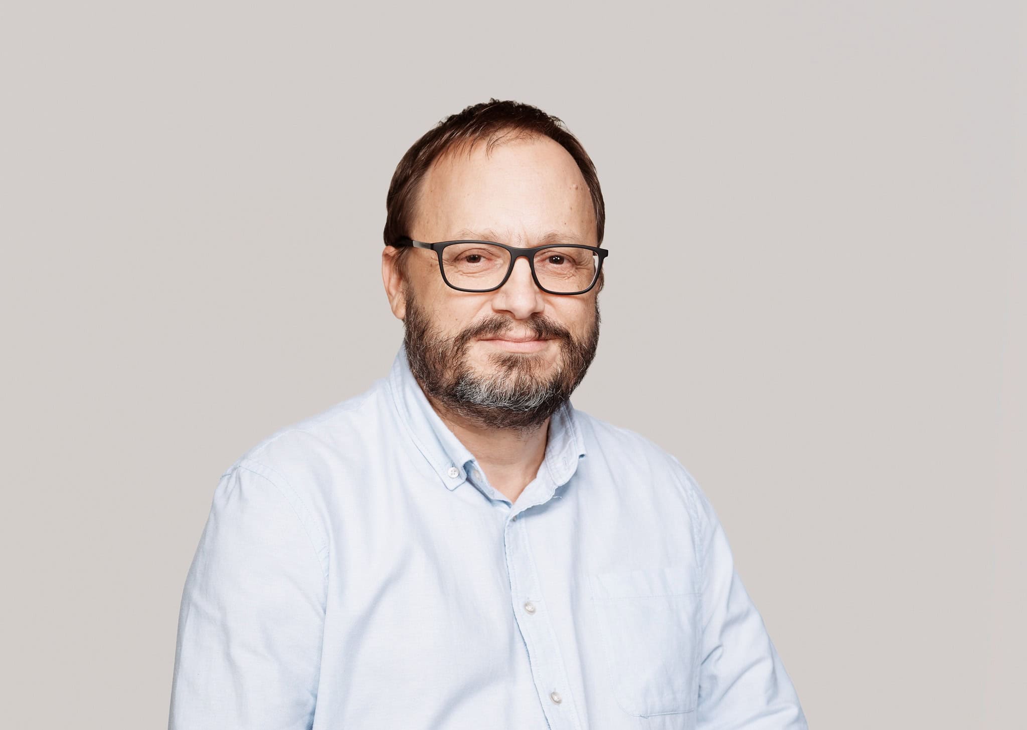 Beruházó férfi portré, szemüveg, hosszú haj, szakáll, kék ing, fehér háttér.