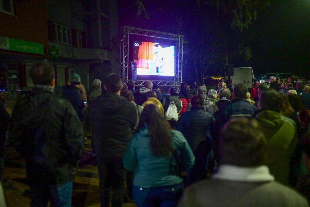 Magyar politikus beszédet tart egy nagyszabású rendezvényen, háttérben a TISZA Párt plakátja.