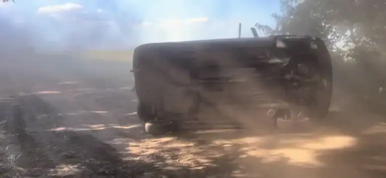 Jármű részben felborulva egy portalanuló útszakaszon, por és fák között, gyors mozdulatokkal mozdulva.