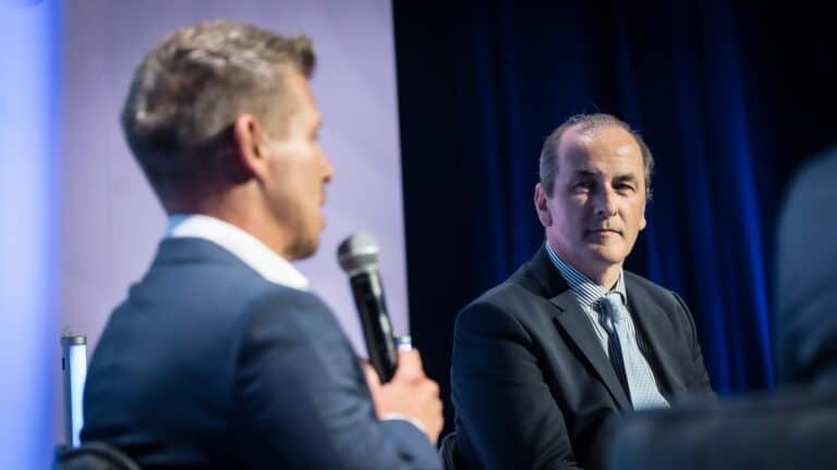 Biztonsági beszélgetés konferencián, két férfi színpadon, üzleti esemény, szakmai vitatkozás, feszültség.