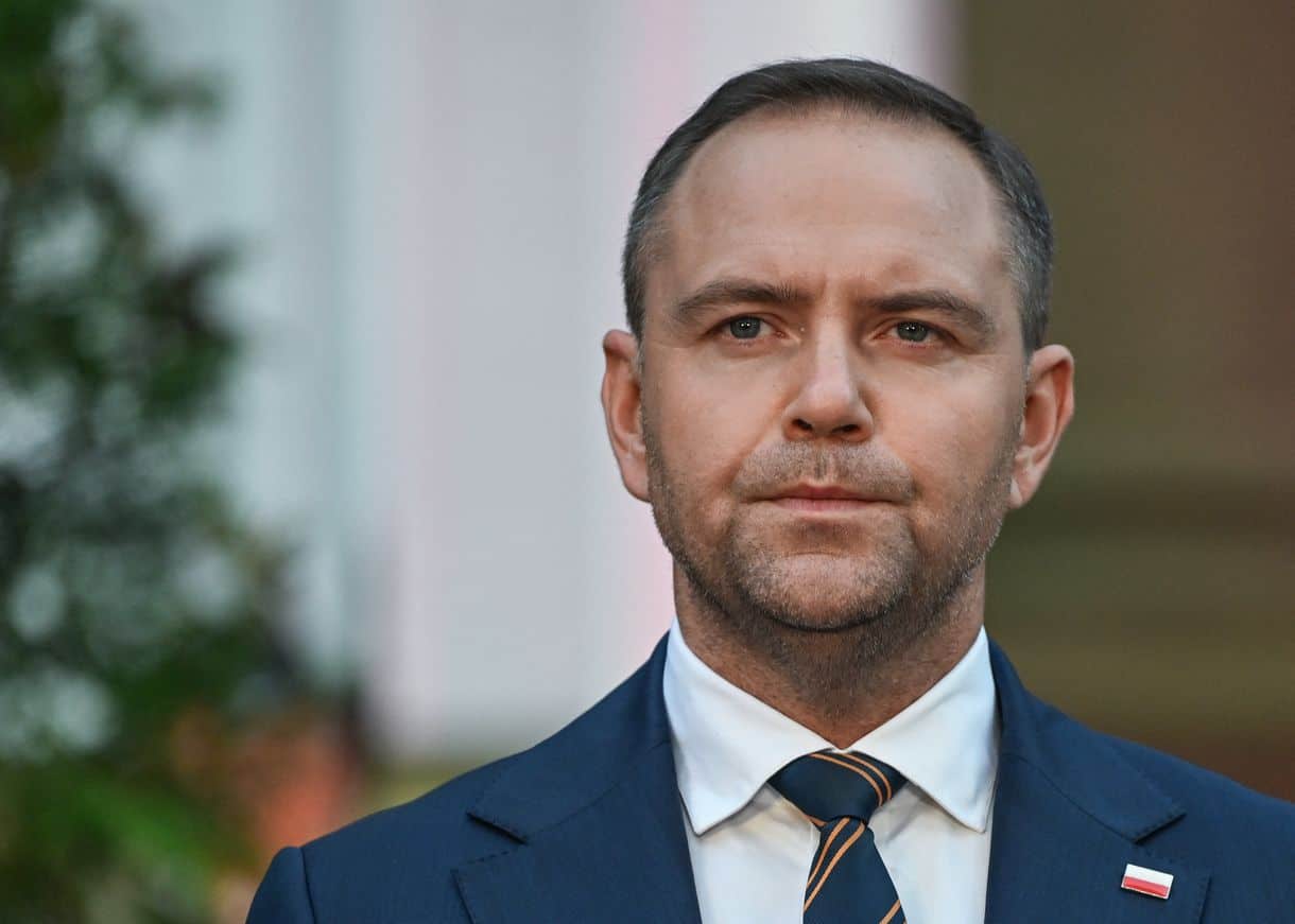 Leíró kép egy férfiról, aki üzleti öltönyben és nyakkendőben ünnepi vagy hivatalos eseményen áll.