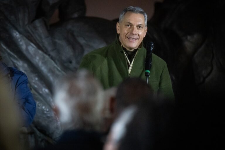 Valóságos portré egy középkorú férfiról, aki egy mikrofont tart, miközben beszél egy sötét, cave-szerű háttér előtt.