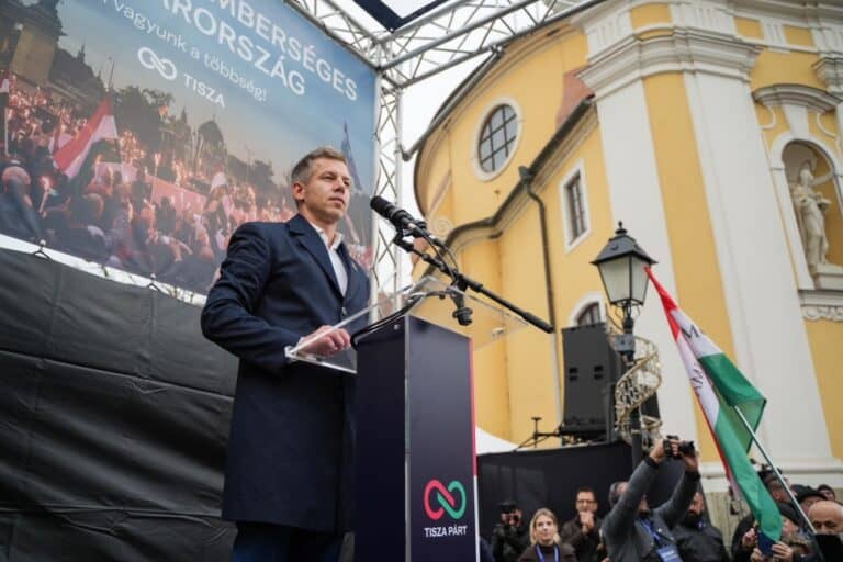 Magyar politikus beszédet tart egy nagyszabású rendezvényen, háttérben a TISZA Párt plakátja.