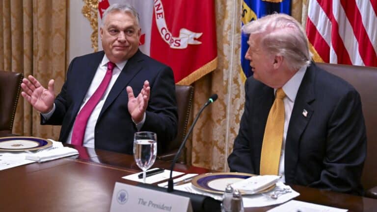 Gazdag politikai megbeszélés két vezető között az asztalnál, háttérben nemzeti zászlók.