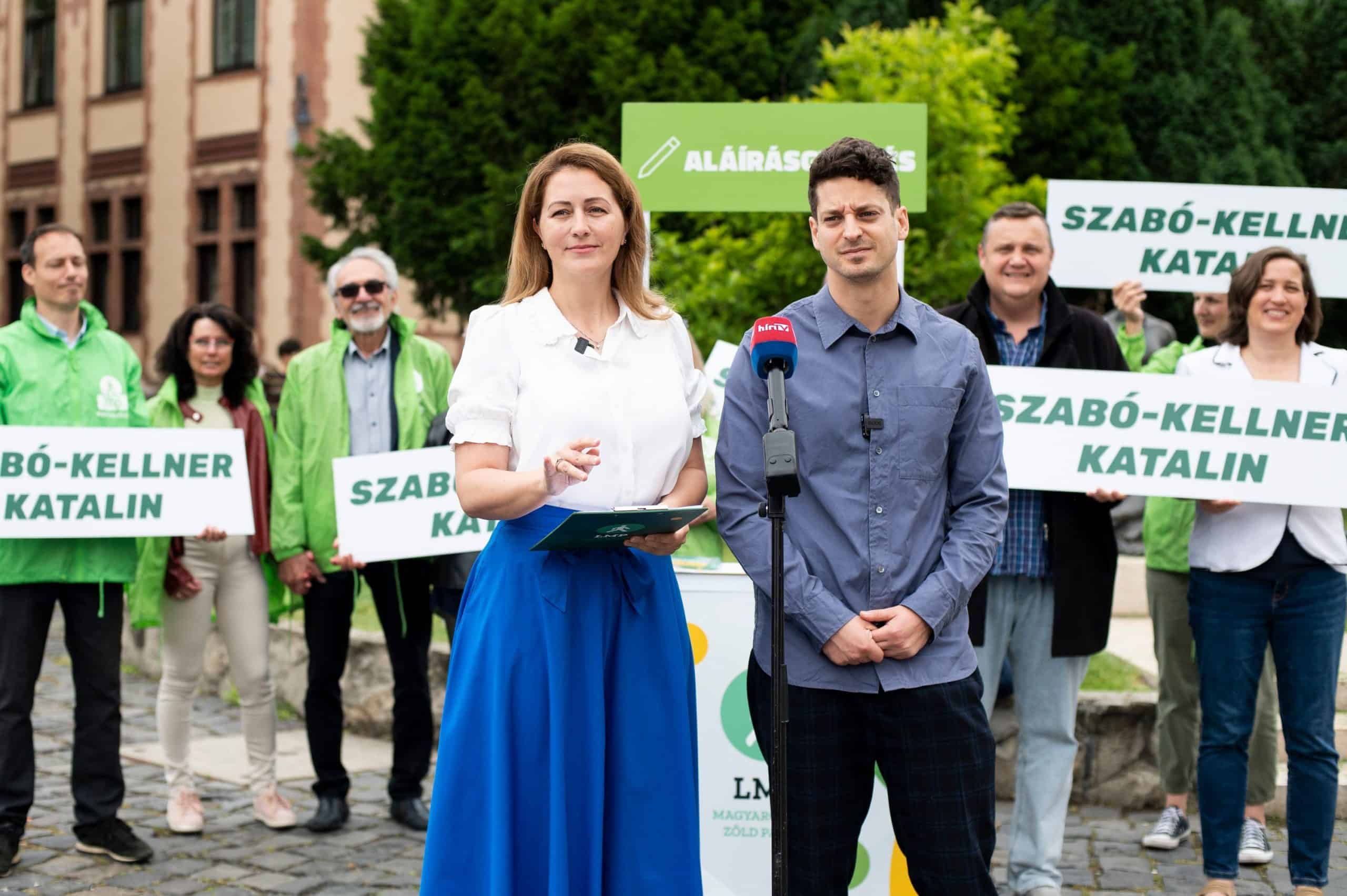 Politikai beszéd, zöld aktivisták tüntetése ülésen, Katalin Szabó-Kellner beszél, háttérben demonstrálók plakátokkal Magyarországon.
