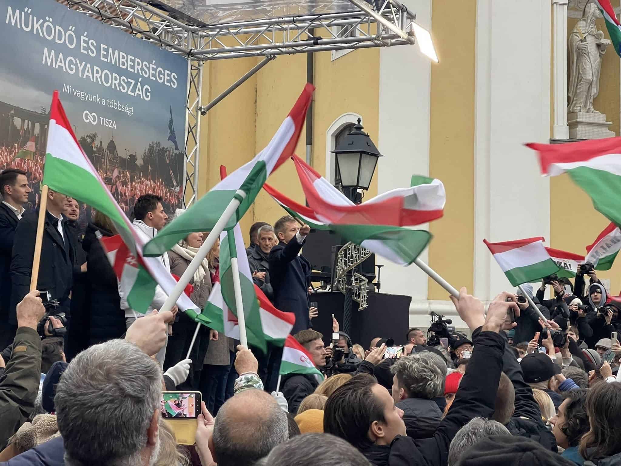 Magyar zászlók emelése egy magyar nemzeti ünnepen az utcán, nagy tömeg előtt.