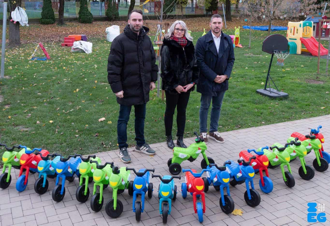 Új gyerekbringák átadása egy közösségi rendezvényen, mosolygós családok és játékok a parkban.