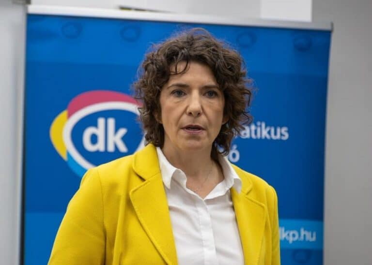 Bartók Andrea, a DK politikusa beszédet tart egy sajtótájékoztatón, háttérben a párt logójával.
