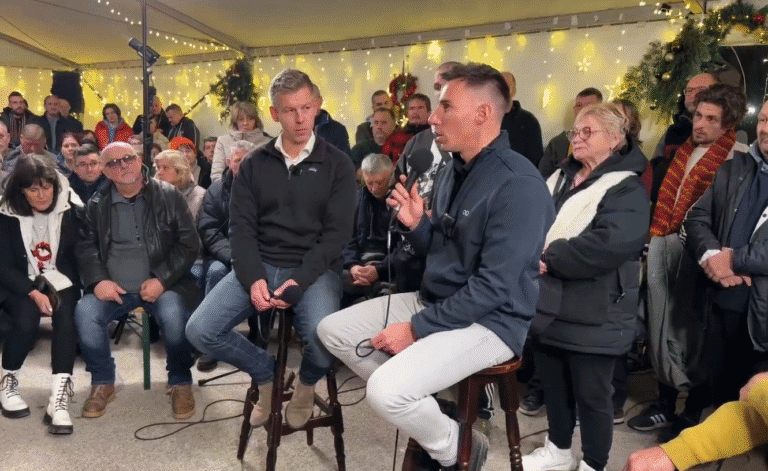 Háttérben ünnepi dekorációk és fények, egy fiatal férfi kérdez egy másik férfit élő közvetítésben egy kérdezz-felelek eseményen.