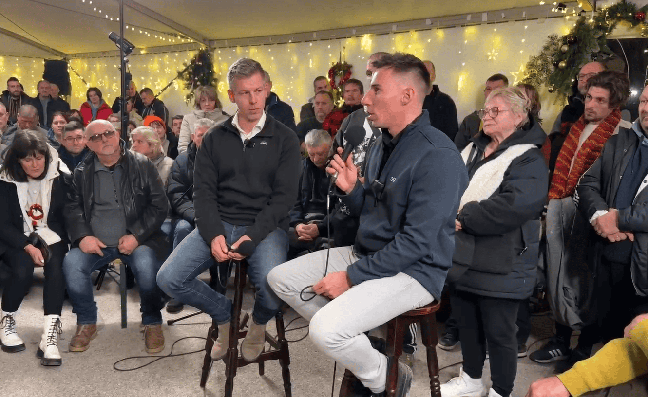 Háttérben ünnepi dekorációk és fények, egy fiatal férfi kérdez egy másik férfit élő közvetítésben egy kérdezz-felelek eseményen.