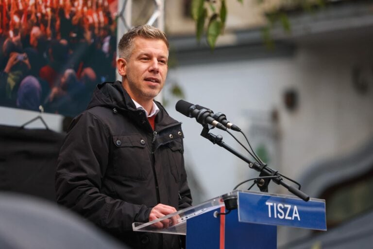 A világ puha újságírója beszédet mond egy kivilágított utcán, egy mikrofon előtt.