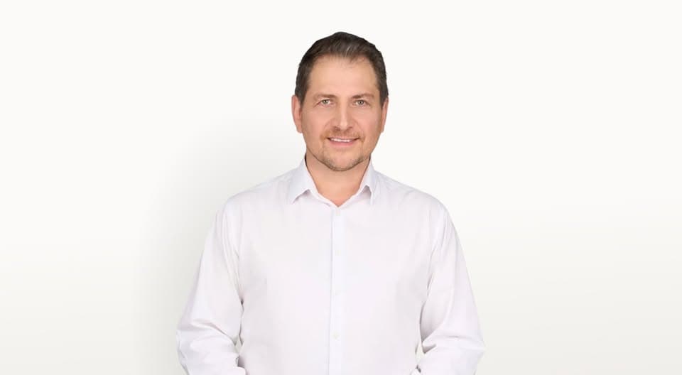 Személy portré egy fehér ingben, mosolyogva, tiszta háttérrel.