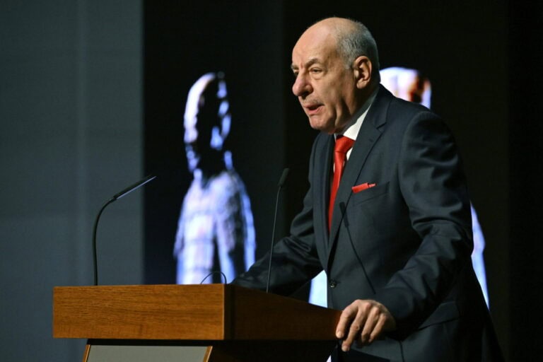 Szakértő politikus beszél egy podiumon meghallgatás közben, kihangsúlyozva fontos politikai kérdéseket.