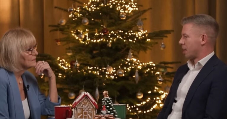 Boldog Karácsonyt egy interjú a magyar médiaportálon Christmas interview with festive decorations in homes and Christmas tree in background.