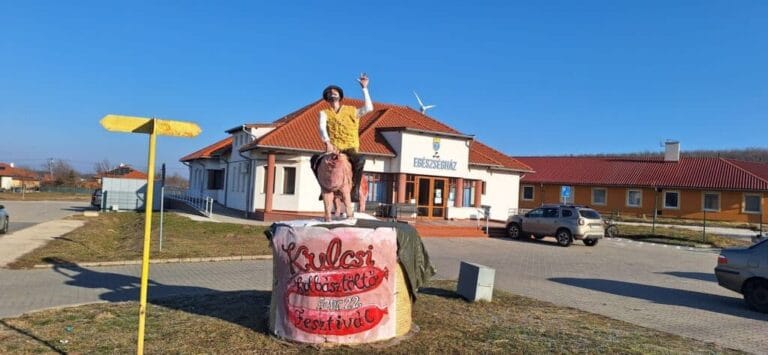 Szabadtéri esemény a faluban, a központi épület előtt a napos időben.