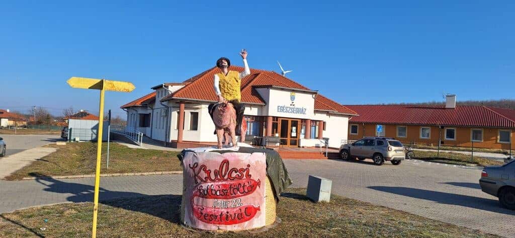 Szabadtéri esemény a faluban, a központi épület előtt a napos időben.
