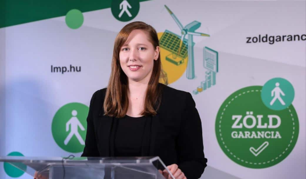 Előadó színésznő egy rendezvényen zöld garancia logóval háttér előtt.