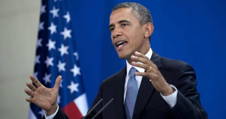 Fekete-fehér amerikai elnök beszéd közben, háttérben amerikai zászló.