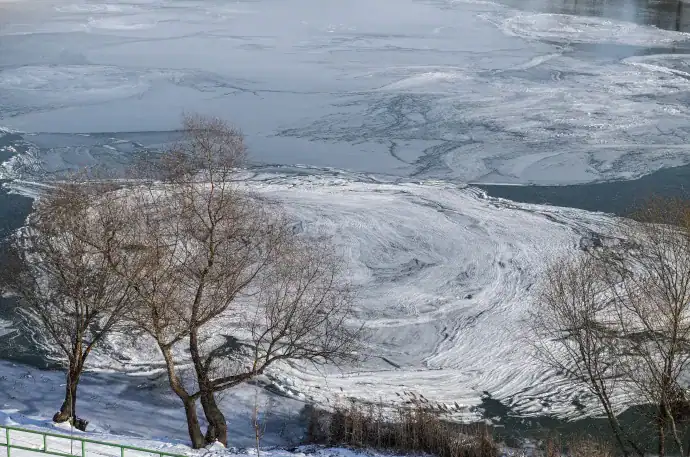 Jégképződés a folyón télen, havas táj, faágak a jég mellett, hideg időjárás Magyarországon.