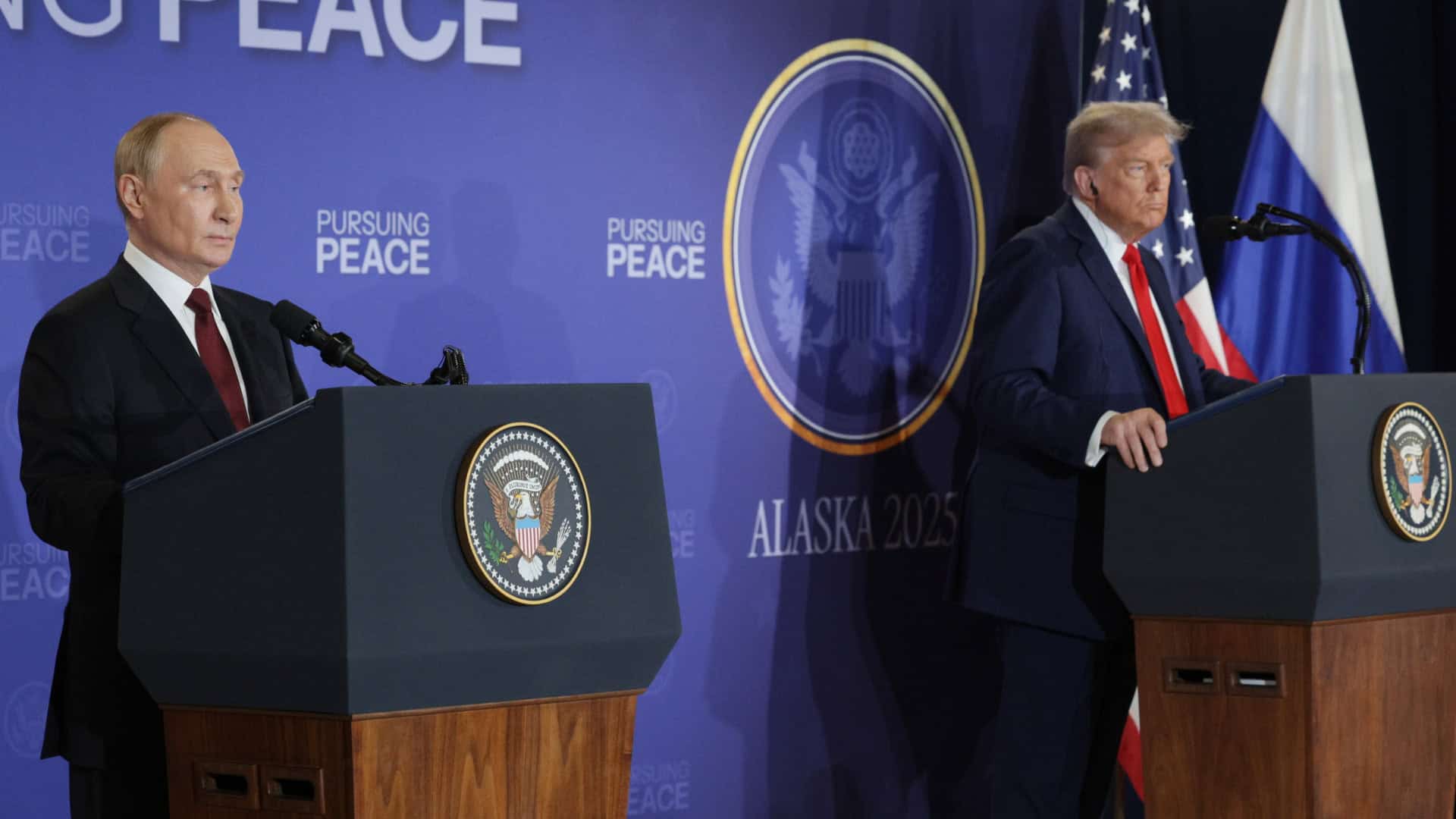 Putyin és Trump egymással szemben, sajtótájékoztató, politikusok, üveg és nemzeti zászlók a háttérben.