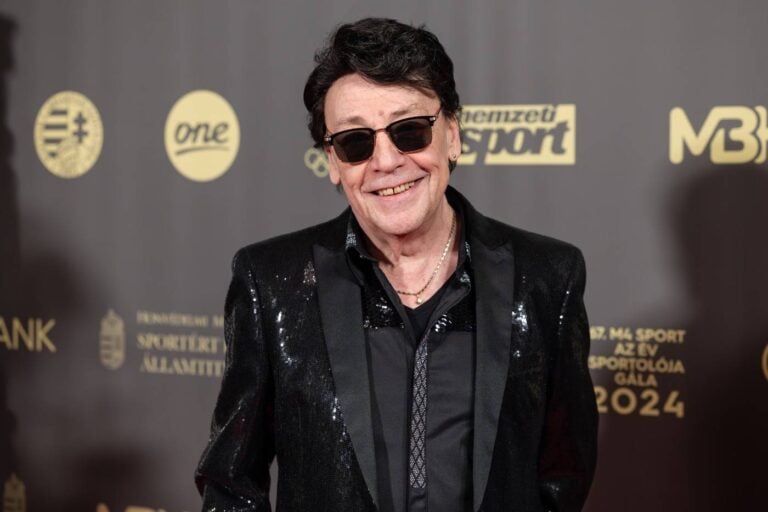 Külső portré egy férfiról, napszemüvegben, fekete öltönyben, vidám arckifejezéssel nagy háttérrel.