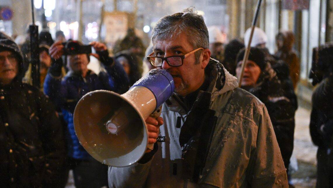 Szervezett tüntetés közben tüntető és médiamunkás a háttérben, szokatlan hangszóróval.