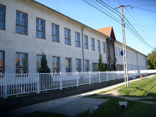 Otthonos iskola épülete a faluban, tiszta és rendezett környezet, diákokkal és tanárokkal.