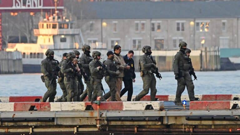 Fegyveres katonák lépnek ki egy hajóról, a háttérben városi épületek és víz látható.