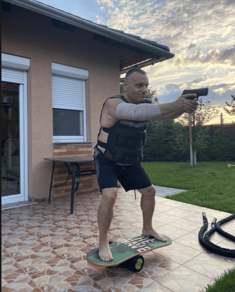 1. Egy férfi lépést tart egy táblás gördeszkán, fegyvert tartva kihívóan az udvaron.