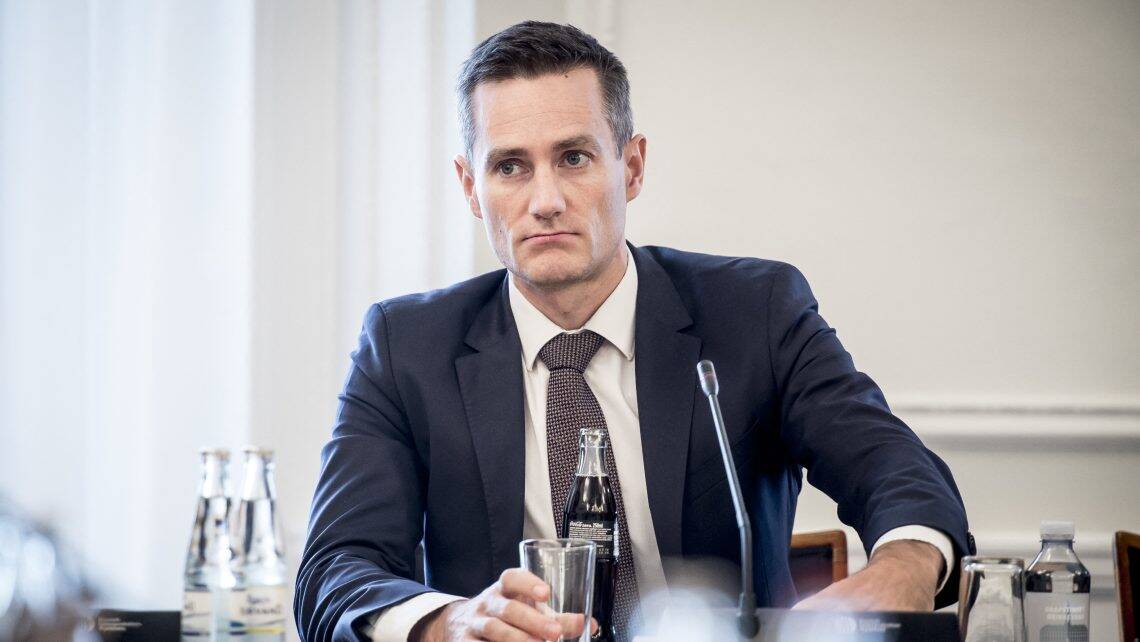 Eltérő hangulatú politikus, aki egy tárgyalóban ül, és mérgesen néz.