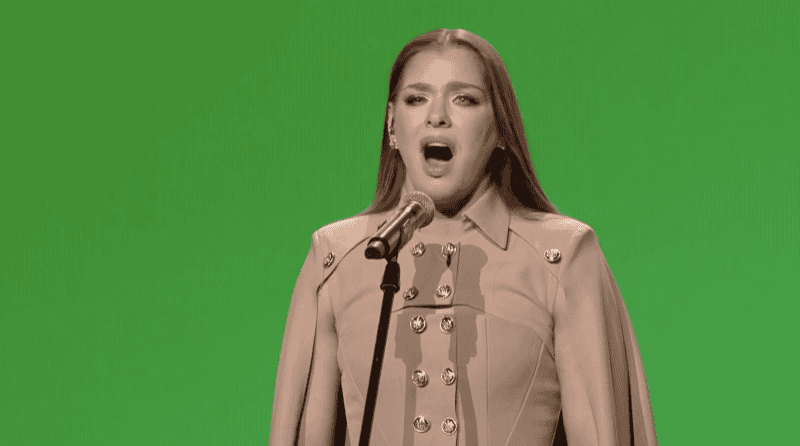 Színésznő énekel élőben mikrofon előtt divatos ruhában háttérzölddel.