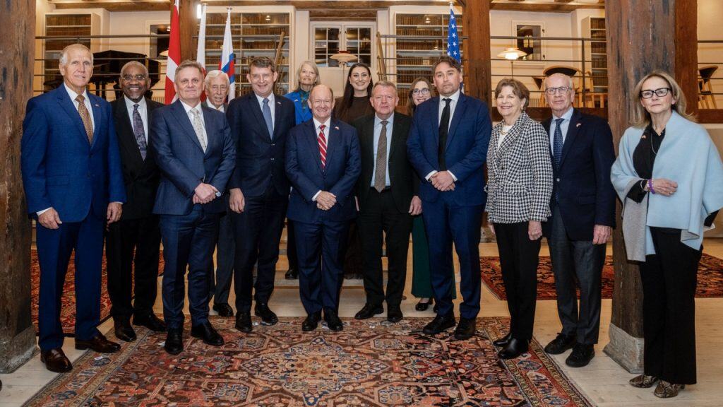 Egy csoport politikus és diplomata fotója egy elegáns, könyves szobában, magyar és amerikai zászlók mellett.