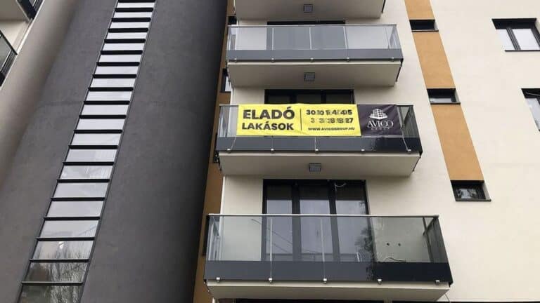 Eladó lakások hirdetése egy modern társasház erkélyénél.