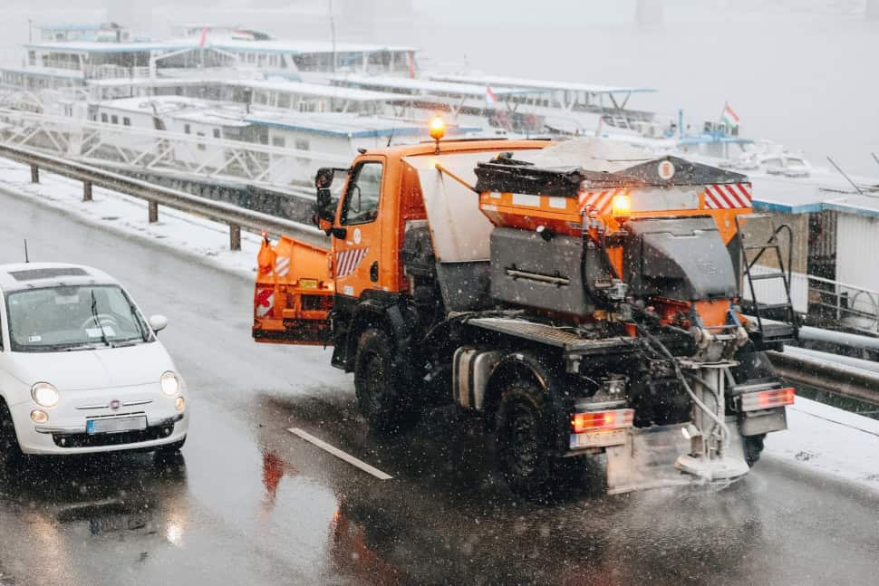 Fűtőgéppel takarítják az utat a téli időjárás miatt, miközben hajók várakoznak a kikötőben.