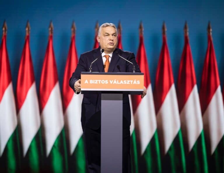 Fidesz politikus a választási kampány során, magyar zászlók mögött beszél.