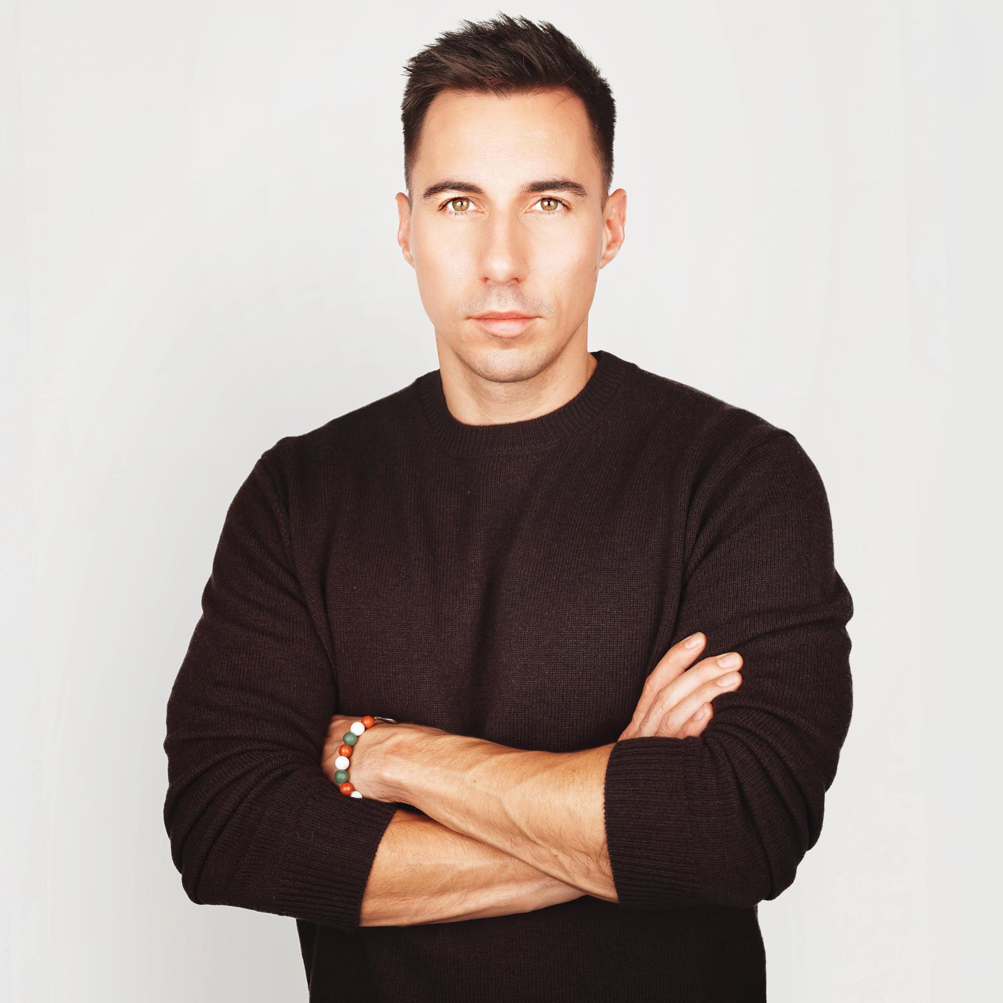 Radnai Márk fekete pulóverben, karjait keresztbe téve, komoly arckifejezéssel néz a kamerába.