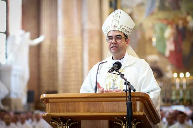 Katolikus püspök beszédet mond a templomban, háttérben vallási szobrok és gyertyák.