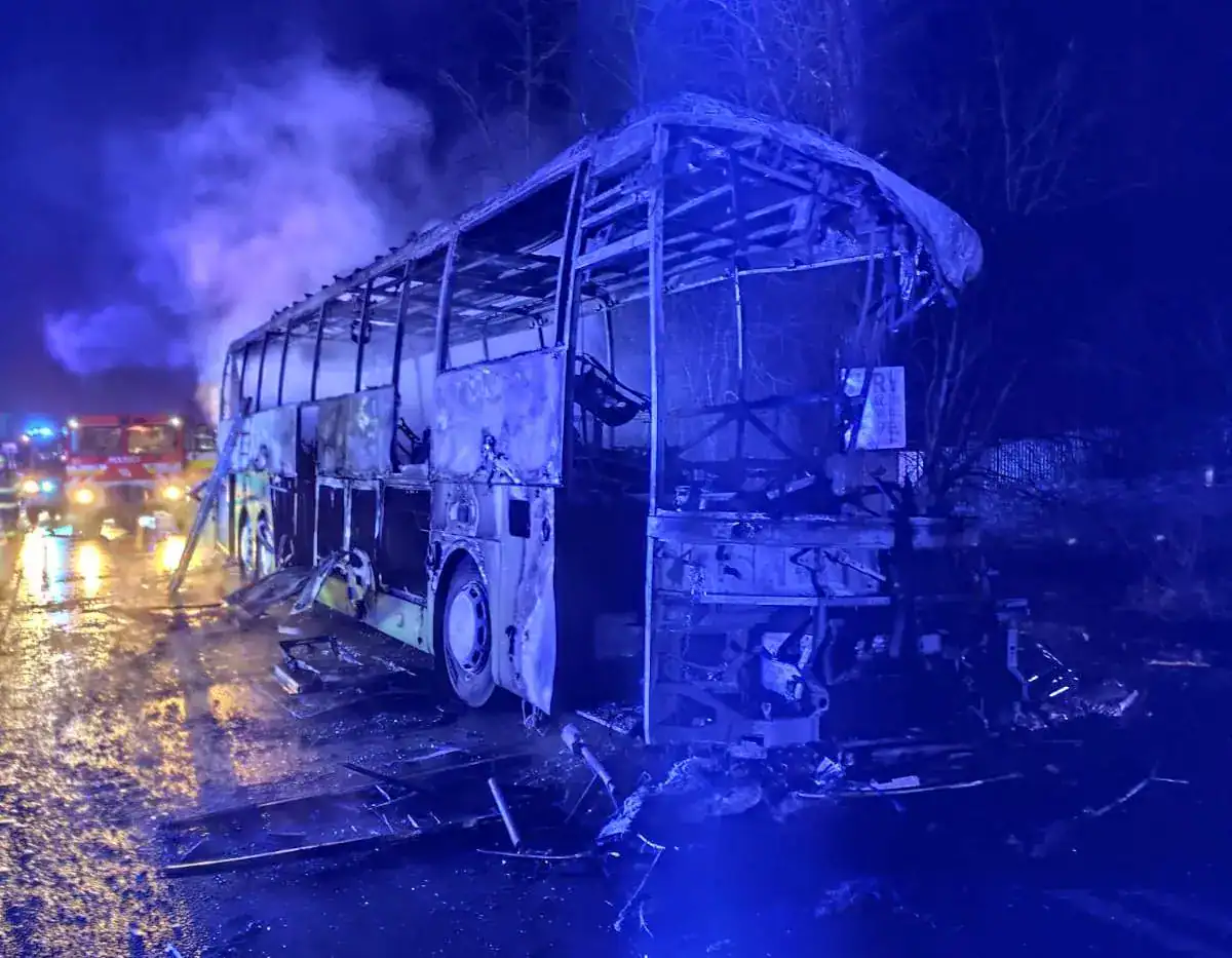 Égő busz és a környező járművek a baleset helyszínén, sötét éjszakai környezetben.