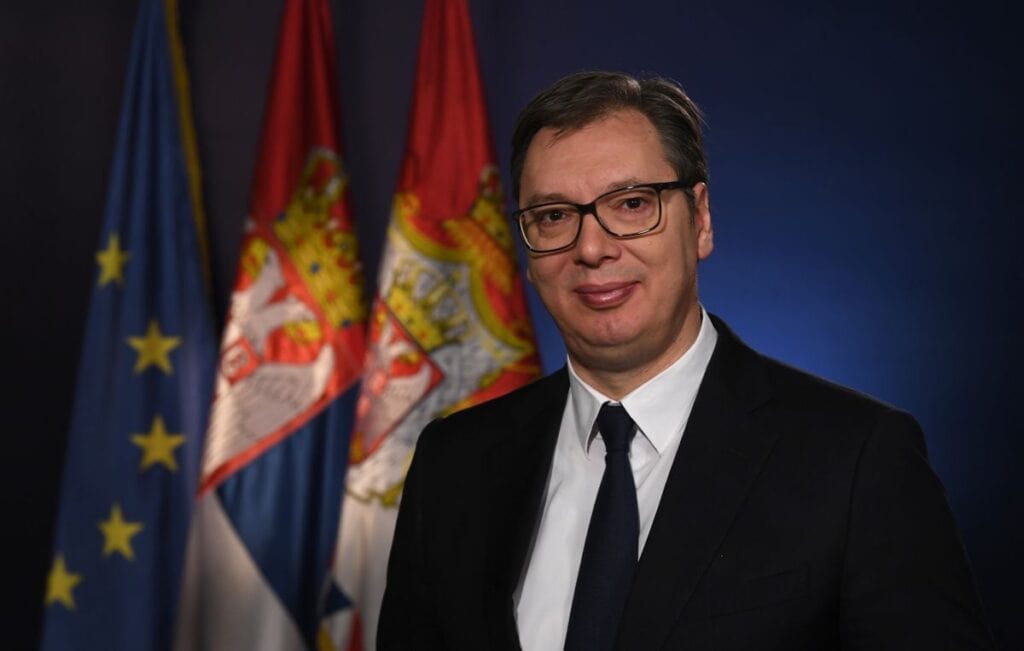 Szerb politikus beszél a háttérben horvát és albán zászlókkal.