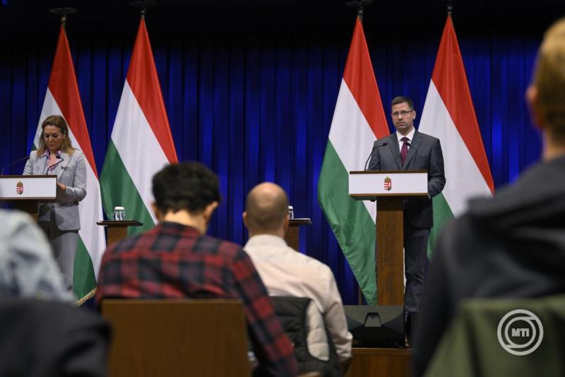 Gulyás Gergely a magyar kormány képviselője, aki sajtótájékoztatót tart, háttérben magyar zászlókkal.