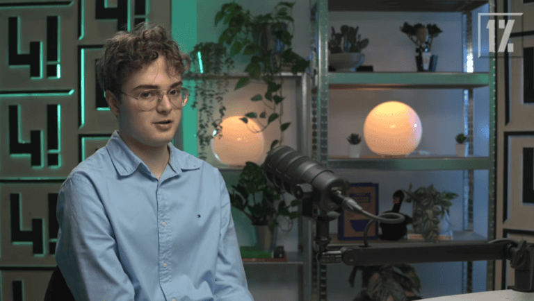 Magyar nyelvű kép, fiatal férfi beszél egy mikrofon előtt, modern stúdióban.