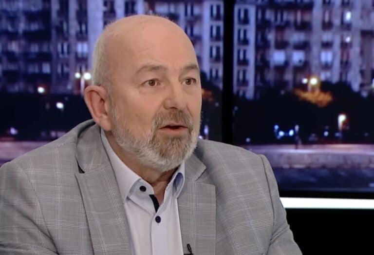 Egy férfi beszél egy tévéműsorban, háttérben városi épületek.