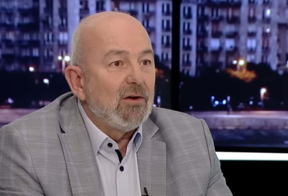 Egy férfi beszél egy tévéműsorban, háttérben városi épületek.