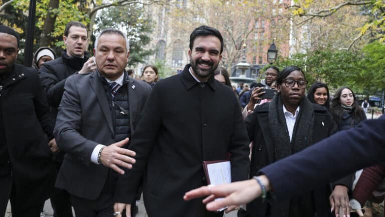 Embercsoport a robbanás helyszínén, nyomozók és médiások a közelben.