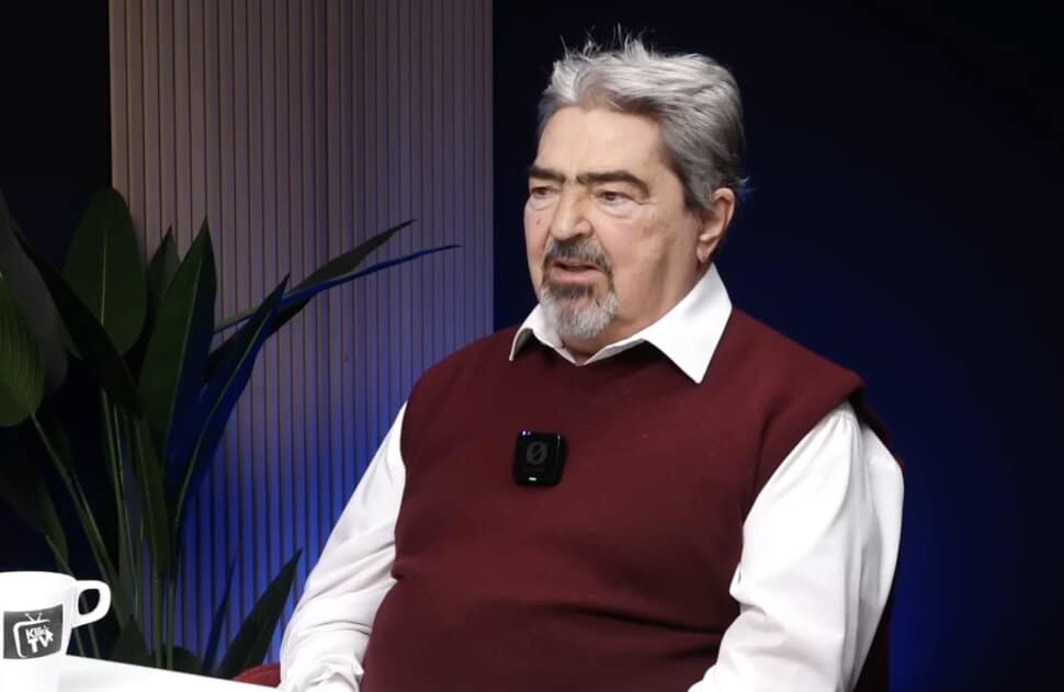 Egy középkorú férfi beszélget egy stúdióban, háttérben növény és modern díszítés.