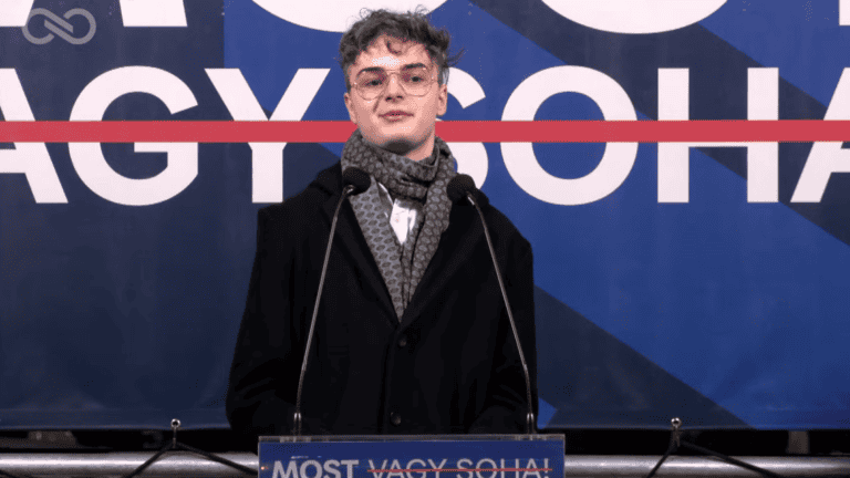 Fiatal férfi beszél egy konferencián, mikrofon előtt állva.