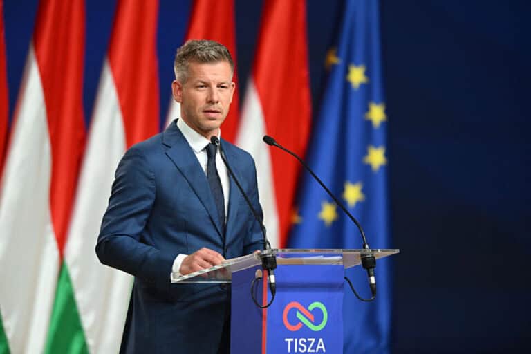 Magyar Péter a nyilvánosság előtt, politikai beszéd közben, háttérben magyar és európai uniós zászló.