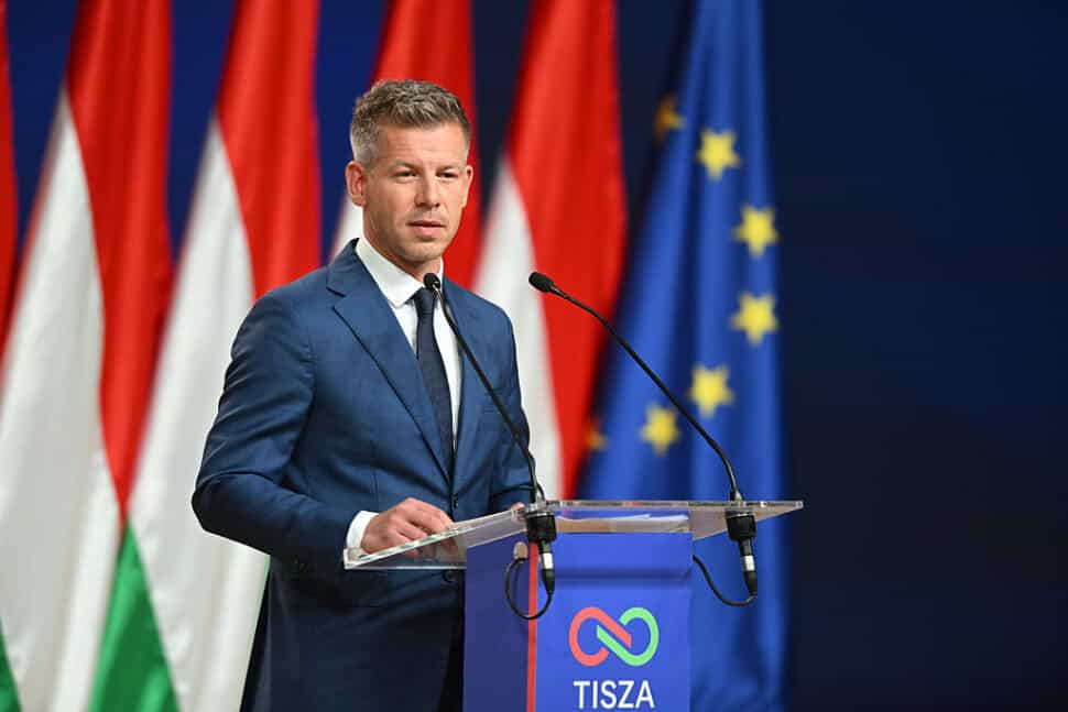 Magyar Péter a nyilvánosság előtt, politikai beszéd közben, háttérben magyar és európai uniós zászló.