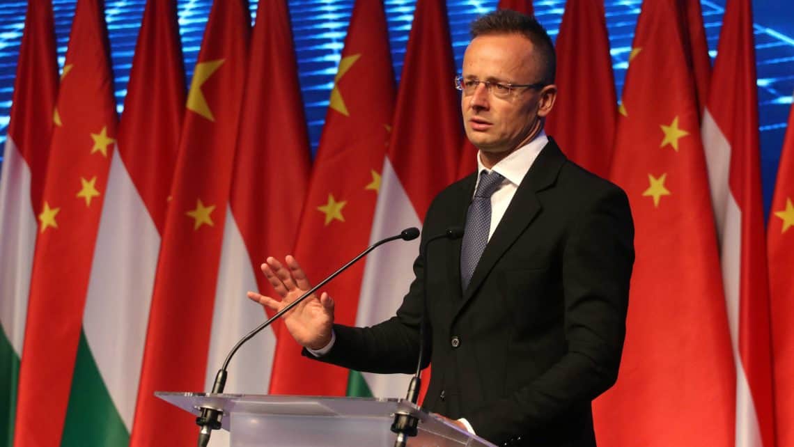 Szijjártó Péter magyar külügyminiszter beszédet tart egy nemzetközi eseményen, háttérben magyar és k.